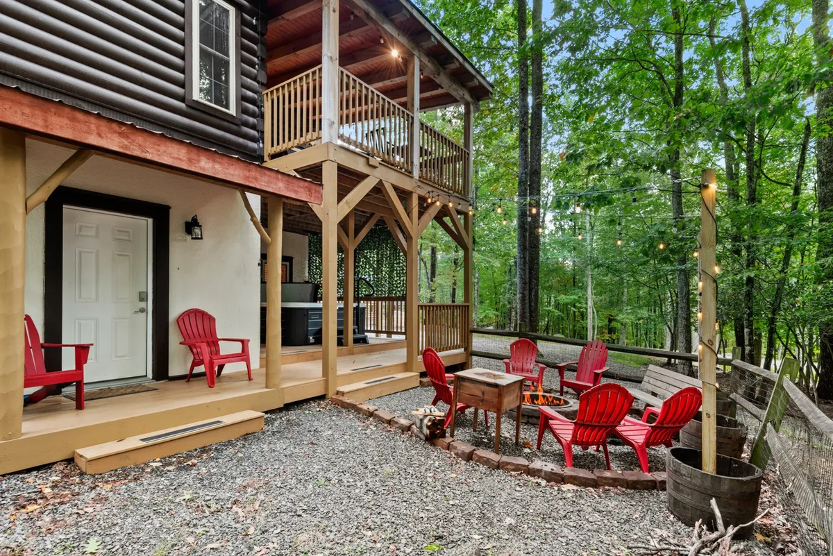 A cozy outdoor scene with red Adirondack chairs gathered around a fire pit, set beside a wooden balcony. The area is surrounded by natural beauty and is perfect for gatherings, storytelling, and stargazing. The fire pit evokes warmth and communal experiences after a day spent outdoors.