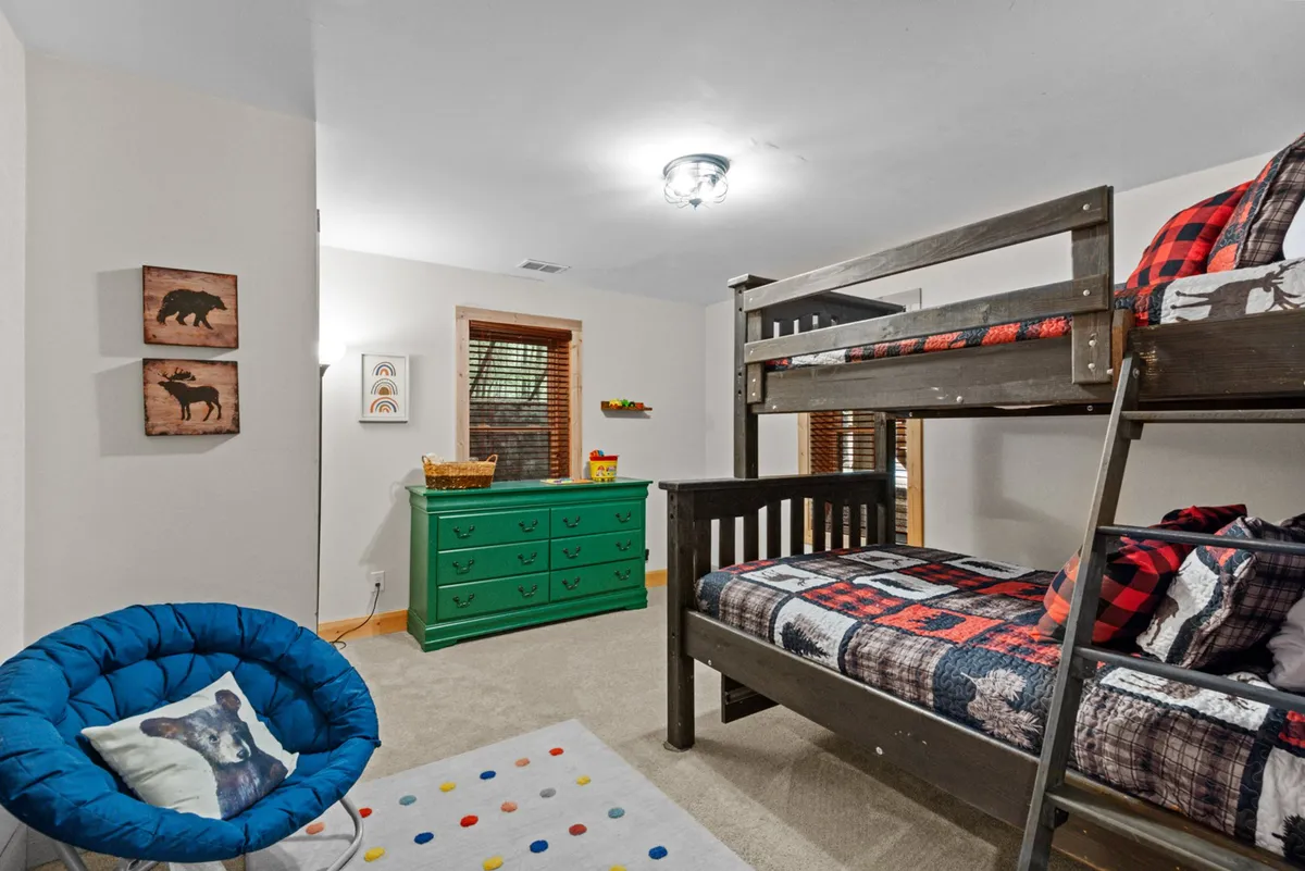A playful children’s bunk room outfitted with colorful bunk beds, a green dresser, a blue chair, and bear-themed wall art. The space feels lively and imaginative, perfect for story time and creative activities.