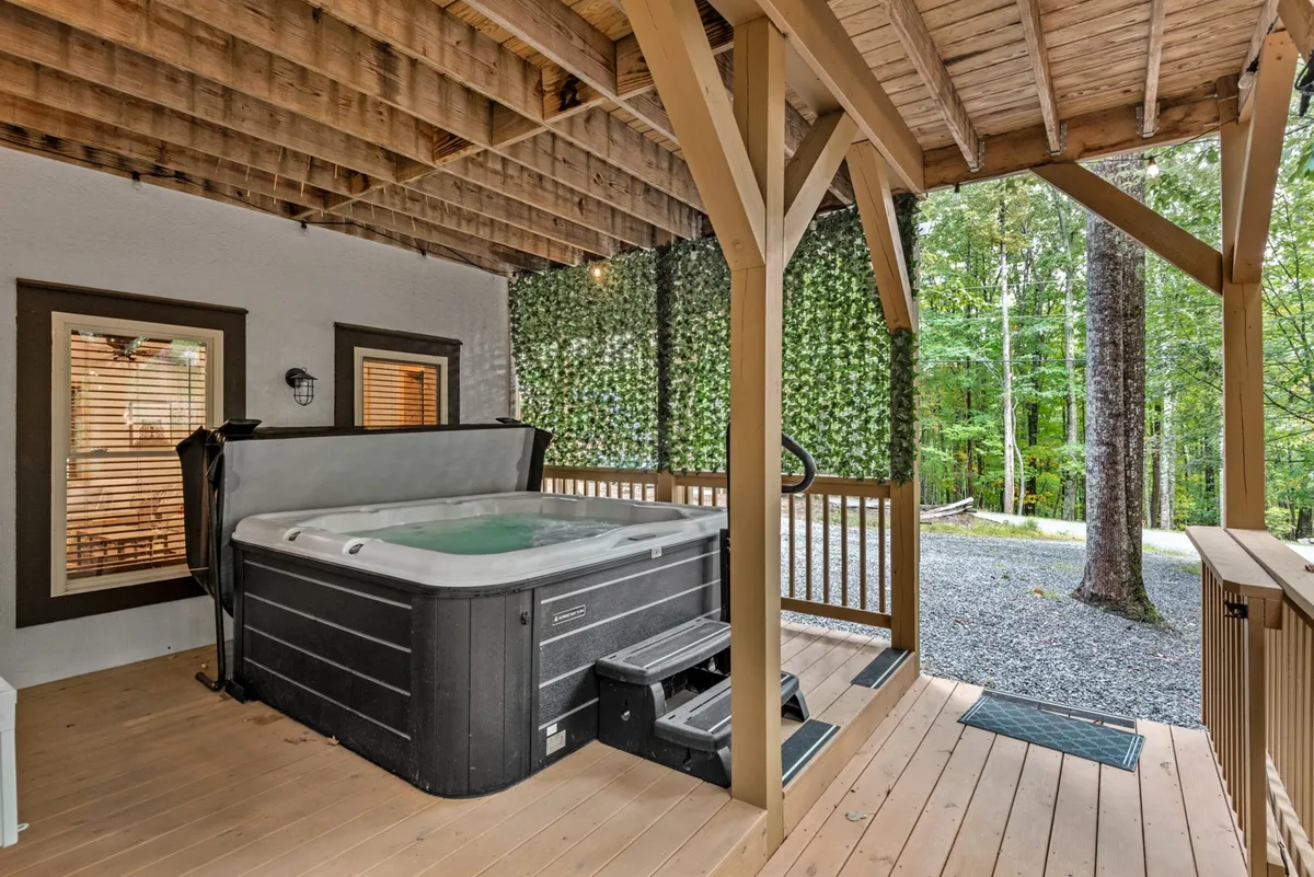 This serene exterior shot features a hot tub nestled beneath wooden beams and beside a lush green wall, suggesting privacy and relaxation. The setup hints at both daytime lounging and nighttime stargazing.