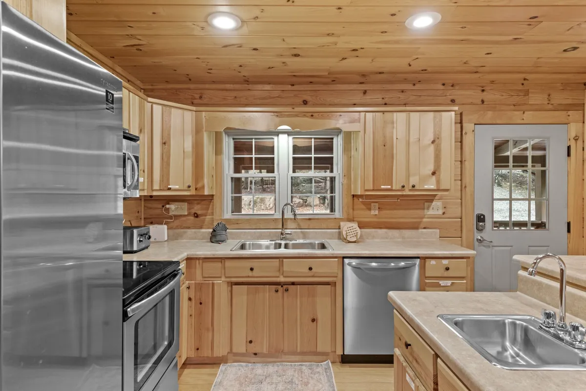 A modern, inviting chef’s kitchen with stainless steel appliances, a double sink with a view, wooden cabinetry, and a spacious kitchen island. The scene radiates warmth and hospitality, perfect for preparing gourmet meals or gathering with friends and family.