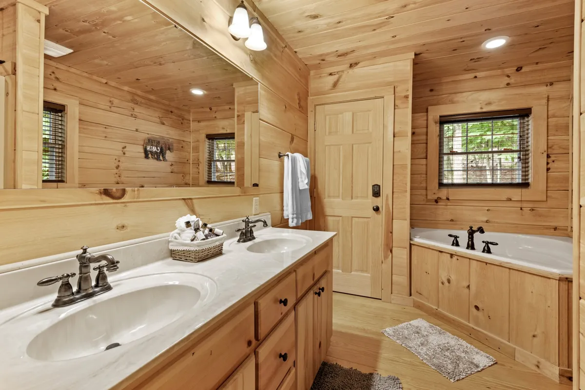 A serene, spacious bathroom with a double sink vanity, natural wood accents, a bathtub, and large mirrors reflecting soft natural light. The space feels spa-like and inviting, perfect for relaxation and morning routines.