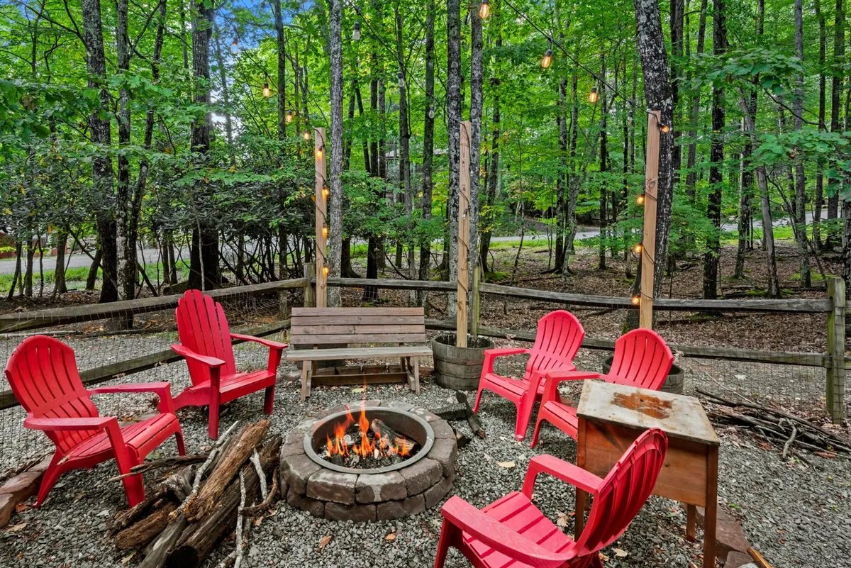 The focus here is a fire pit surrounded by red chairs and a wooden bench, illuminated by string lights above. The space exudes a cozy, communal vibe perfect for family gatherings, storytelling, and enjoying evenings outdoors under the stars.